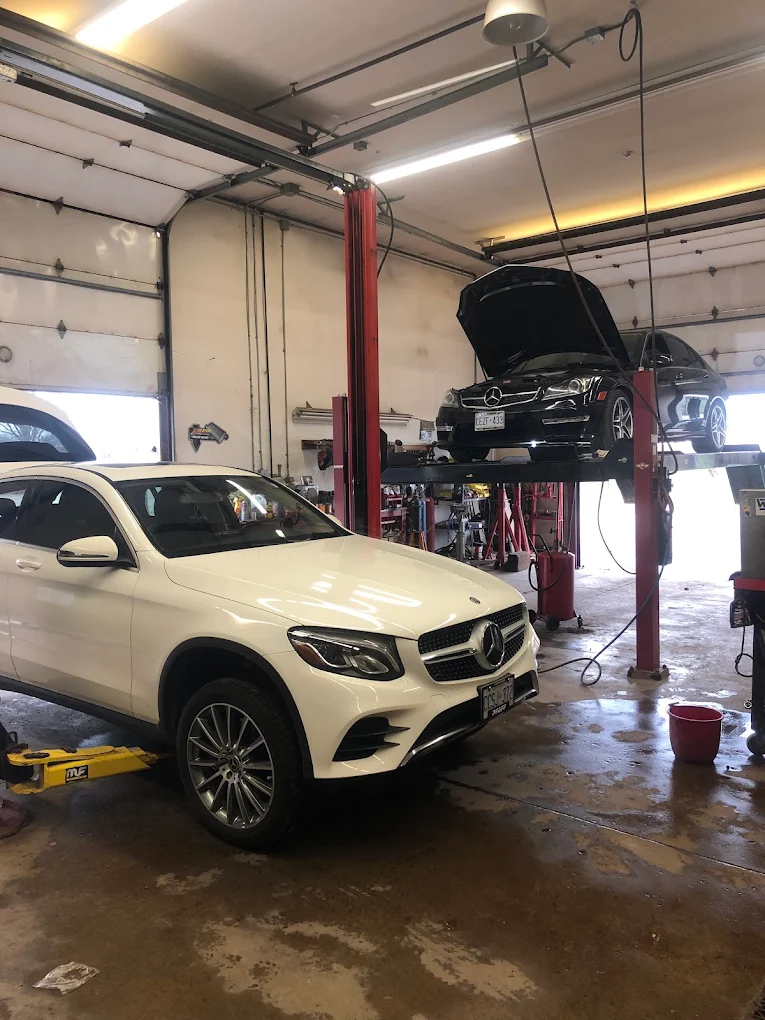 Two service bays at Pete's Muffler with a Mercedes SUV on the floor and a Mercedes sedan raised on the hoist