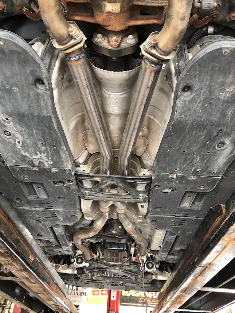 Corroded factory exhaust and heat shields on the underside of a vehicle raised on the hoist