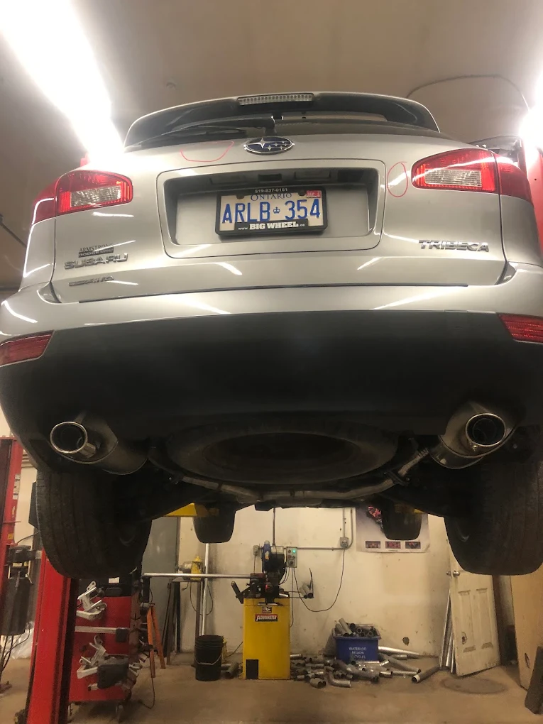 Subaru on the hoist at Pete's Muffler with the tire balancer and racks of pipe stock behind it
