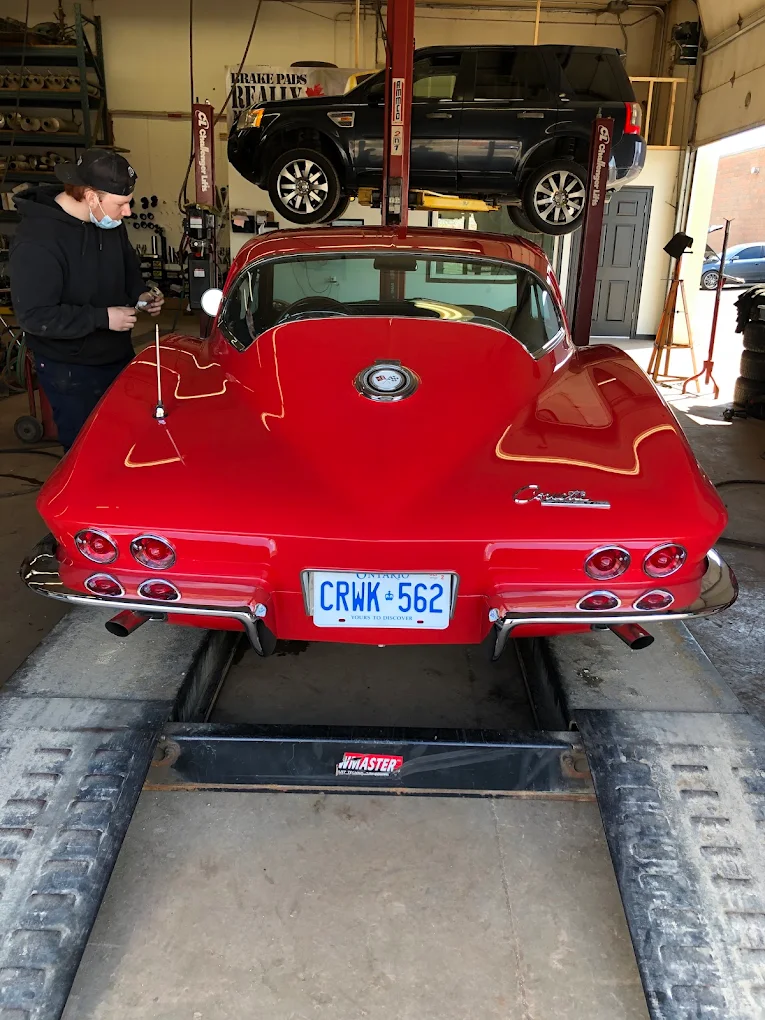 Technician working on a classic red Chevrolet Corvette on the drive-on lift at Pete's Muffler in Guelph